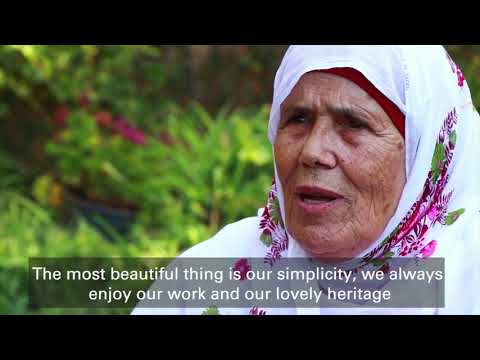 Oudere Palestijnse vrouw in traditionele kleding spreekt over Maftoul uit Palestina - Traditionele Palestijnse Couscous | Handgerold, met groene tuin op de achtergrond.
